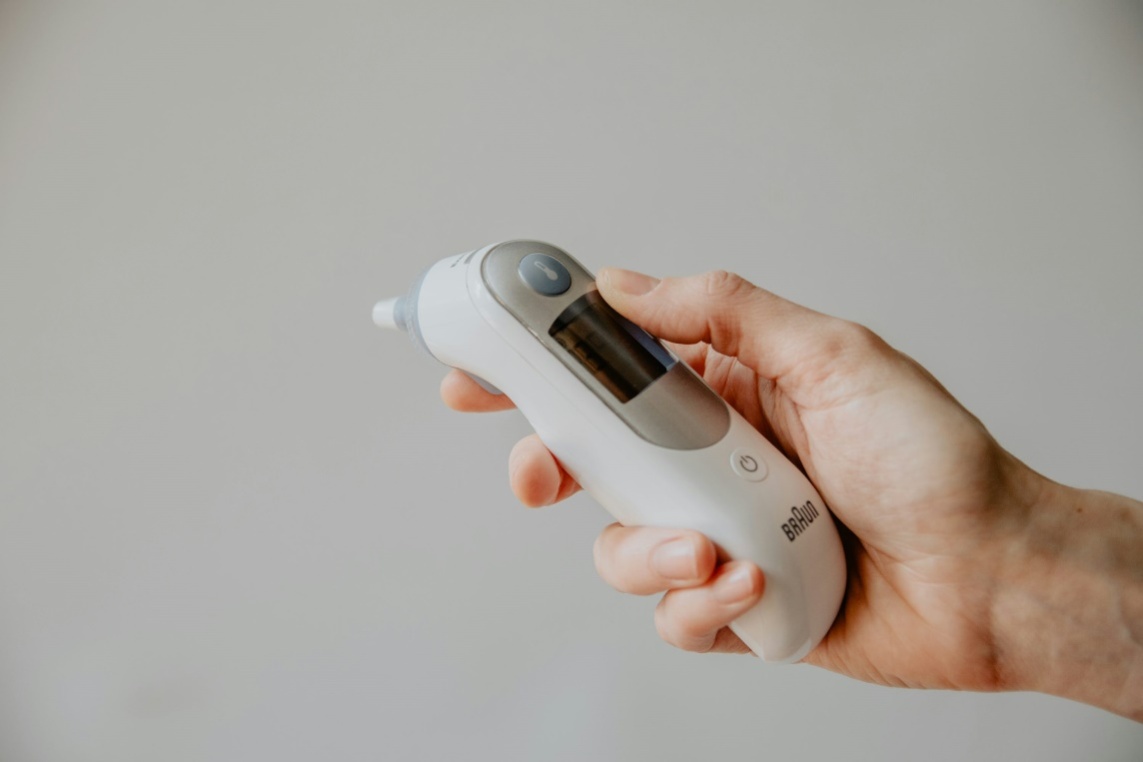 A person holding a thermometer, symbolizing the decision-making process regarding sickness