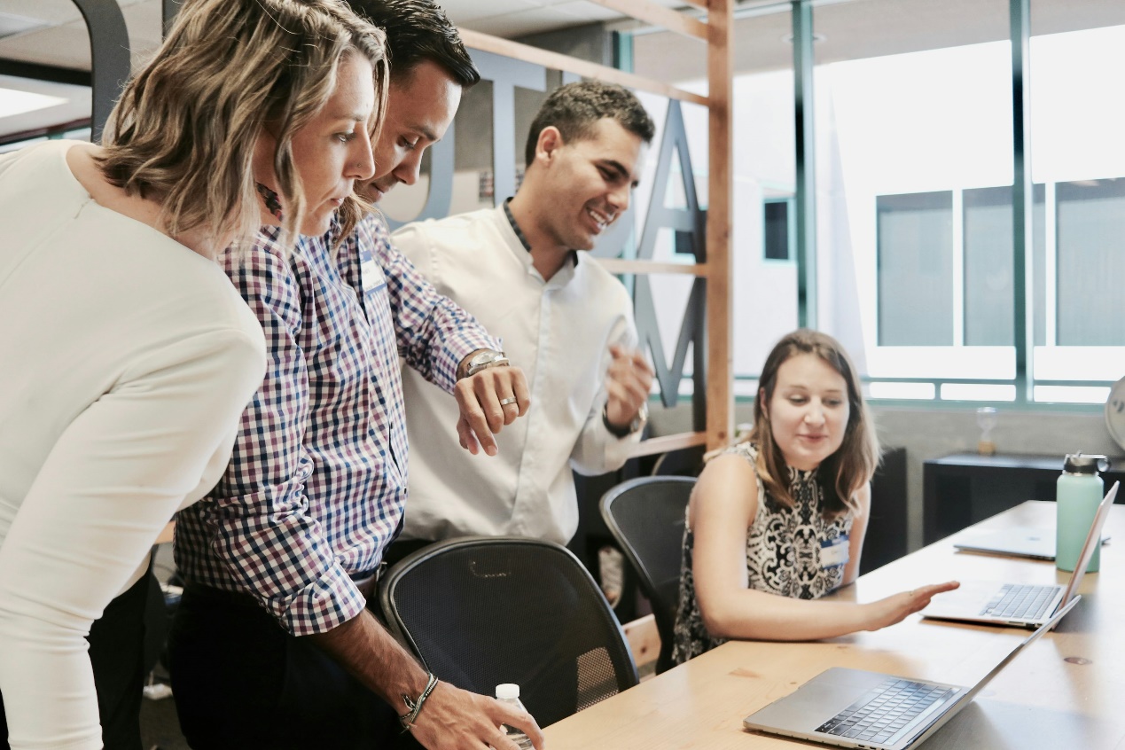 Three employees standing at a table of another employee with laptops on it