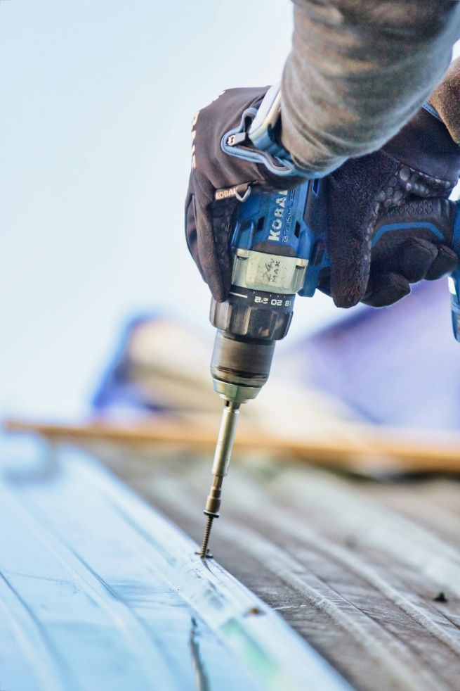 A person using a drill to drill a piece of wood, representing the hands-on nature of construction projects.