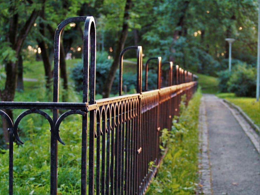 Decorative black metal fence along a park pathway surrounded by lush greenery.