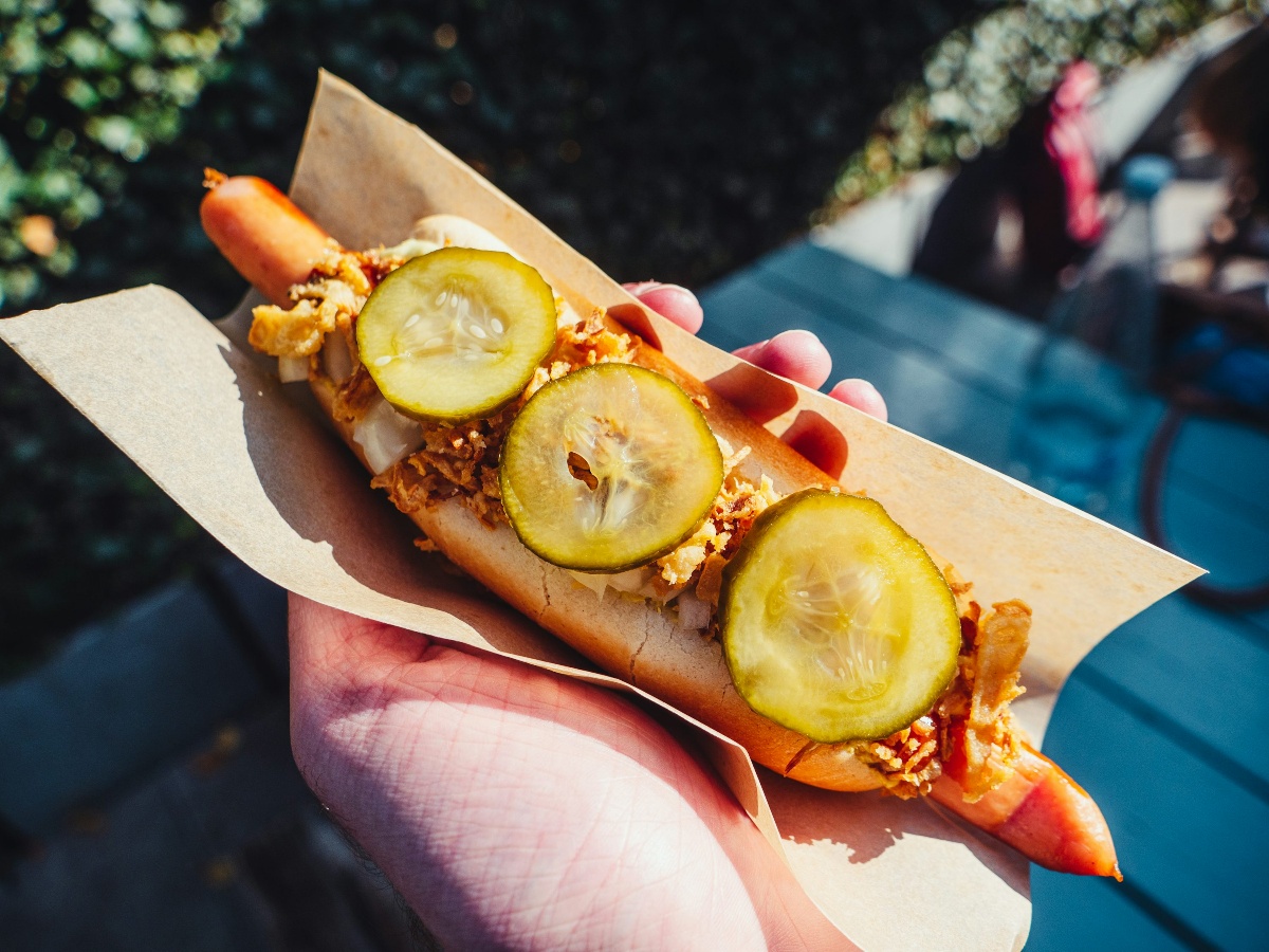 A gourmet-style hot dog topped with pickles and crispy onions served at a local festival