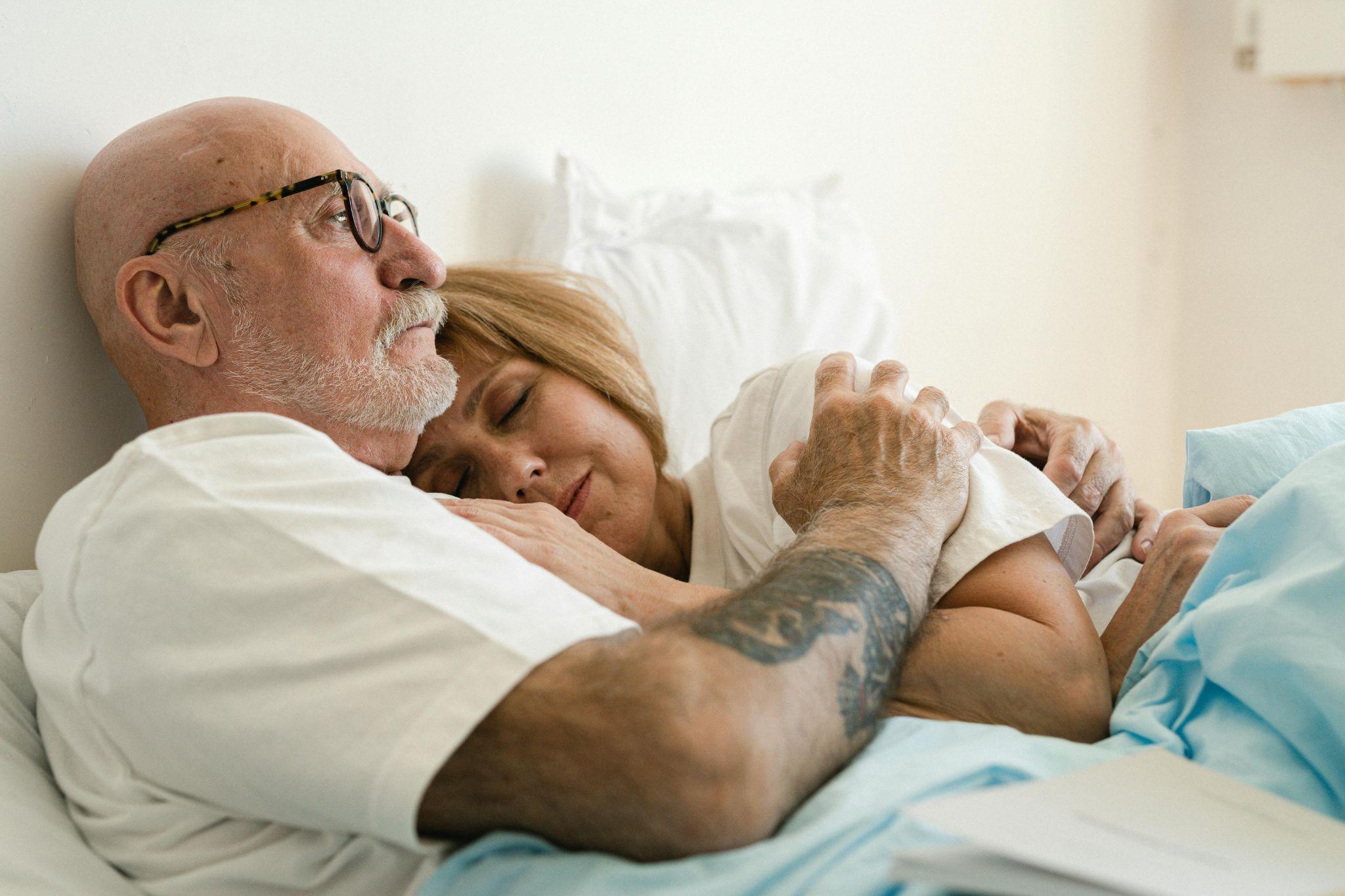 Older man and woman resting together under blankets in bed.