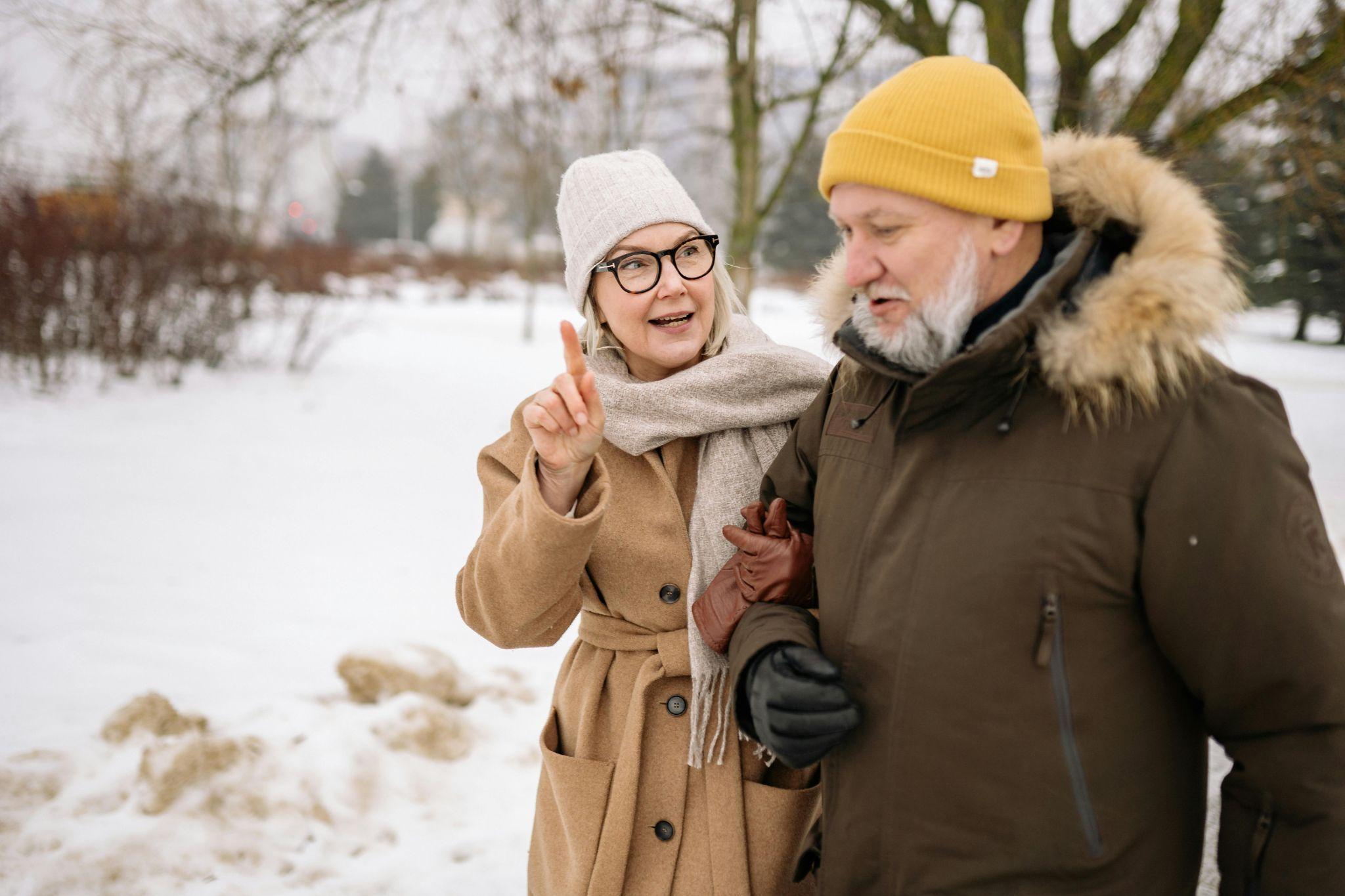 A senior couple bundled in winter clothing walking together in the snow.