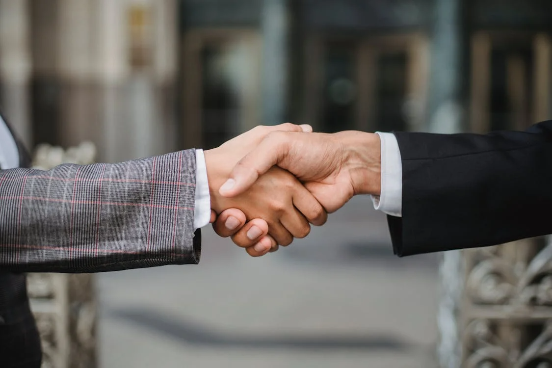 Two people in business attire shake hands, symbolizing agreement or partnership.
