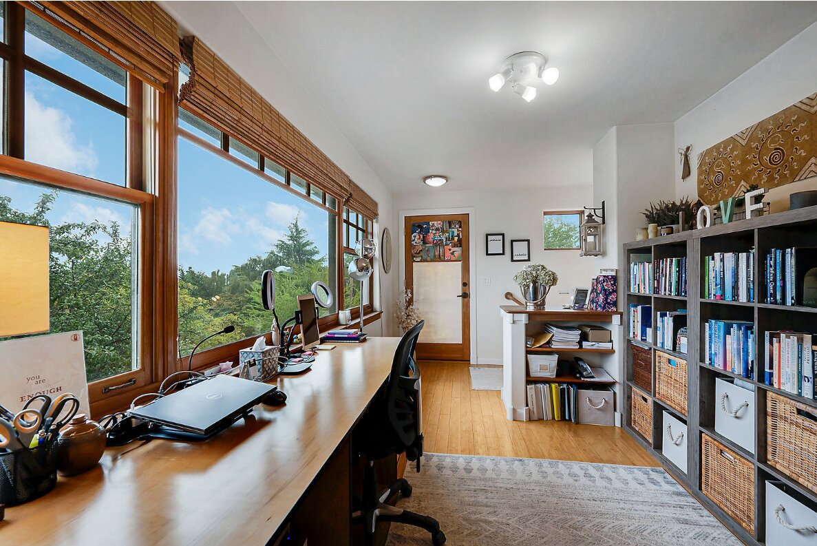 A home office with a long desk, windows, and built-in bookshelves