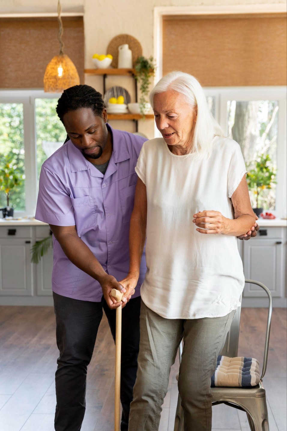 caregiver helping a senior woman walk safely at home to support mobility and independence