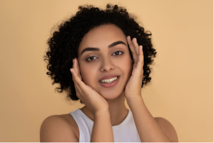 Smiling woman with clear, glowing skin touching her face gently.