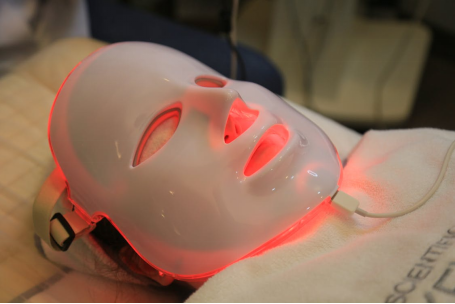 Patient lying down wearing an LED light therapy mask during a facial treatment.